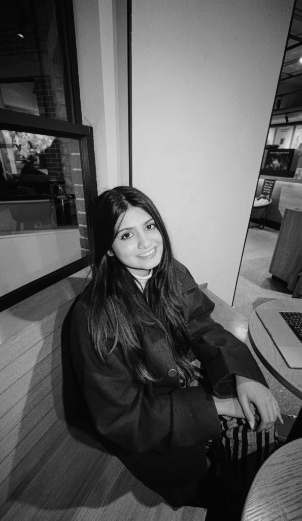 Radha seated at a café table, smiling toward the camera