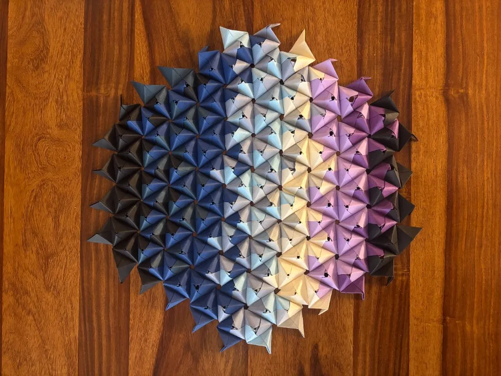 Modular origami mosaic in a blue-to-cream gradient on wood