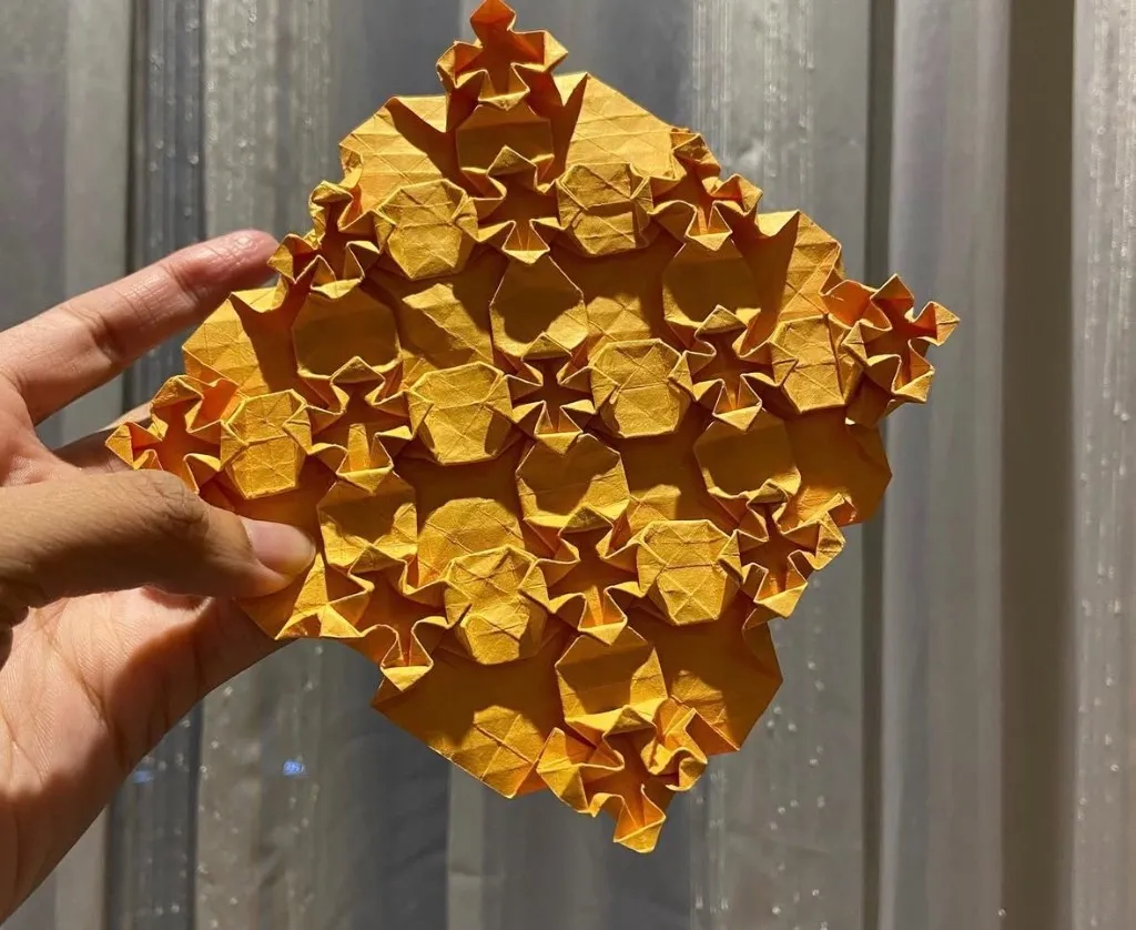 Hand holding a bright orange origami tessellation with star folds